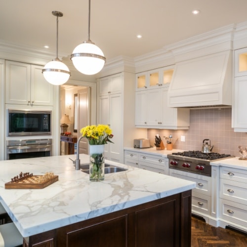 A white and clean kitchen with a large island topped with calacatta marble