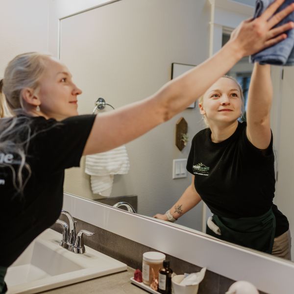 Rise and Shine female house cleaner wipes the bathroom mirror